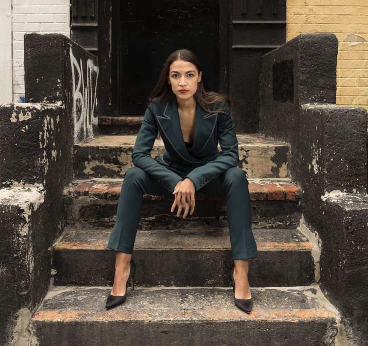 This meme is an image of Alexandria Ocasio-Cortez, a U.S. politician, sitting on a stoop with a serious expression. The text overlay on the image reads "Me when I'm told I'm not allowed to use the stairs". The meme is likely poking fun at the idea that people are being told to use the stairs instead of the elevator, implying that they are being treated like children.