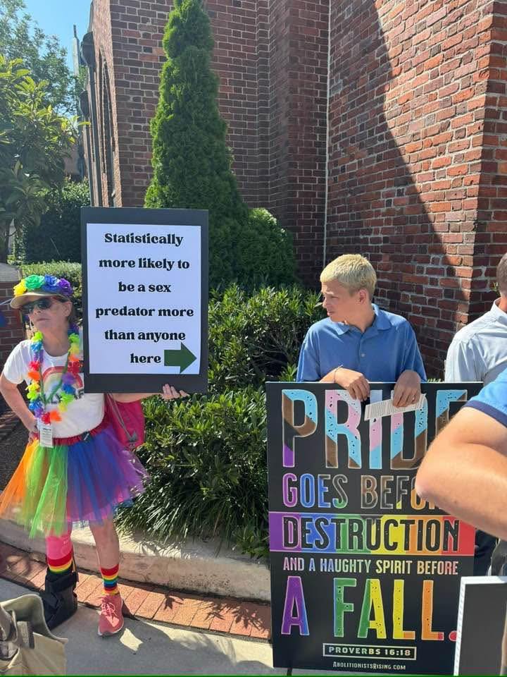 The meme features a person dressed in rainbow attire, holding a sign that reads, "Statistically more likely to be a sex predator than anyone here." They are surrounded by other individuals, one of whom is holding a sign that says, "PRIDE GOES BEFORE DESTRUCTION AND A HAUGHTY SPIRIT BEFORE A FALL." The image is likely intended to be humorous or ironic, as it juxtaposes the celebratory atmosphere of Pride Month with a message that is often associated with religious or conservative viewpoints. The contrast between the two signs creates a sense of irony and playfulness, making the image a humorous commentary on the intersection of Pride Month and religious or conservative values.