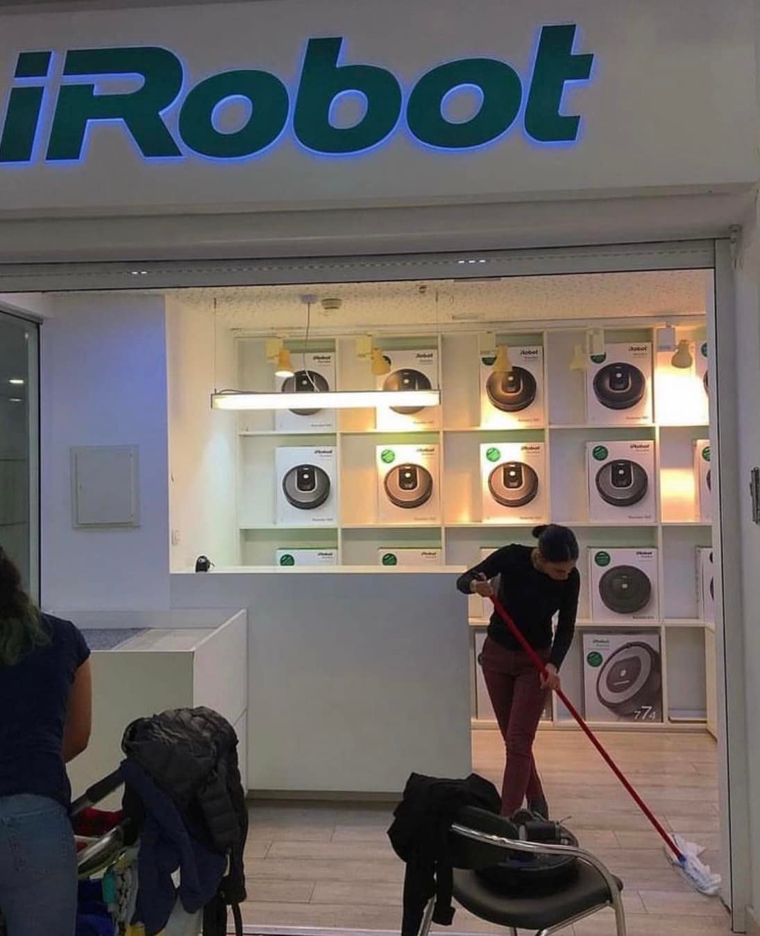 This meme is an image of a storefront with a sign reading "iRobot" (a company that makes robots for cleaning homes) with a sign in the window that says "Help Wanted". The implication is that the company that makes robots to clean homes is now looking for human help, suggesting that their robots are not living up to expectations.