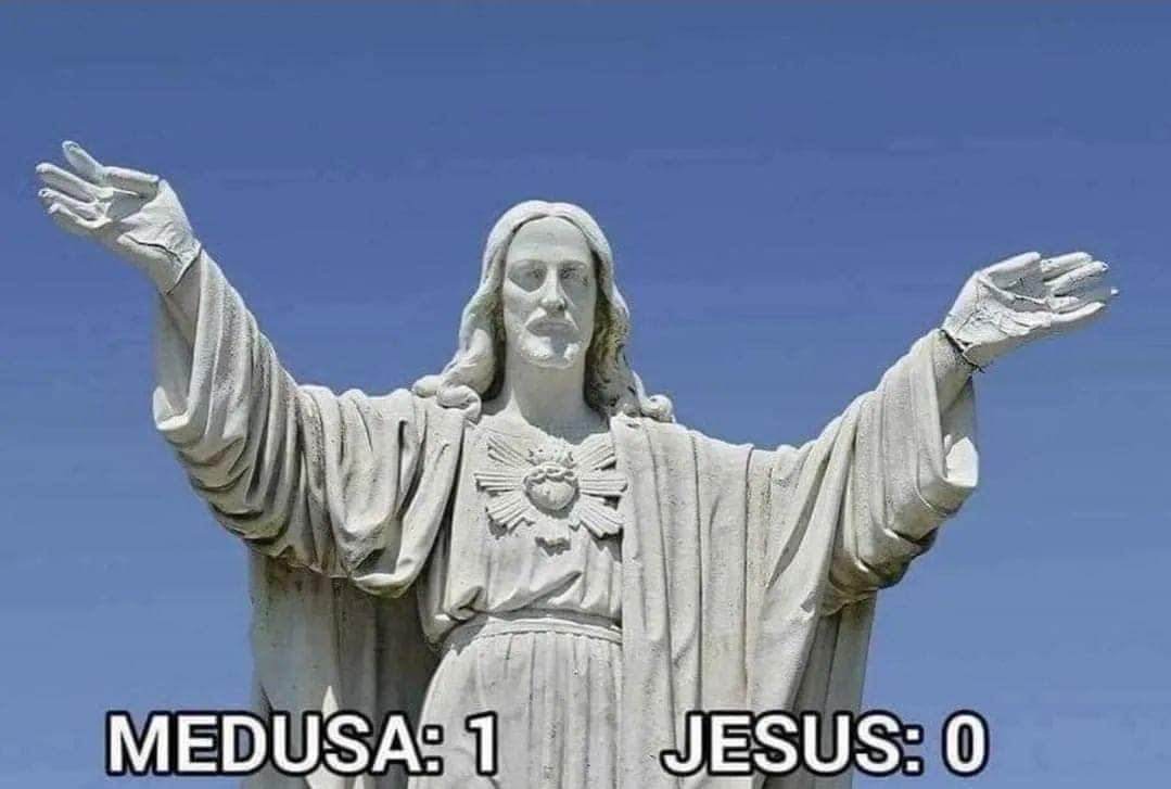 This meme is a play on the phrase "it's all in the family" and features a split-screen image of the Statue of Christ with the head of a lion (the Christ/Lion hybrid from the movie "Excalibur") on the left, and the head of a lion with the body of a man on the right. The text "Medusa: 1 / Jesus: 0" appears below the image.