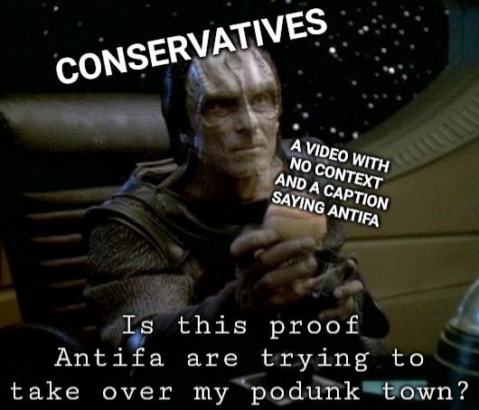 This meme is an image of a character from the Star Trek franchise, likely a Klingon warrior, with a caption that is a quote from the character. The quote reads: "In 2-3 sentences, describe this meme for someone who cannot see it. Include any text that appears in the image." The meme is a humorous take on the typical instructions for describing an image, and the quote is a self-referential joke.