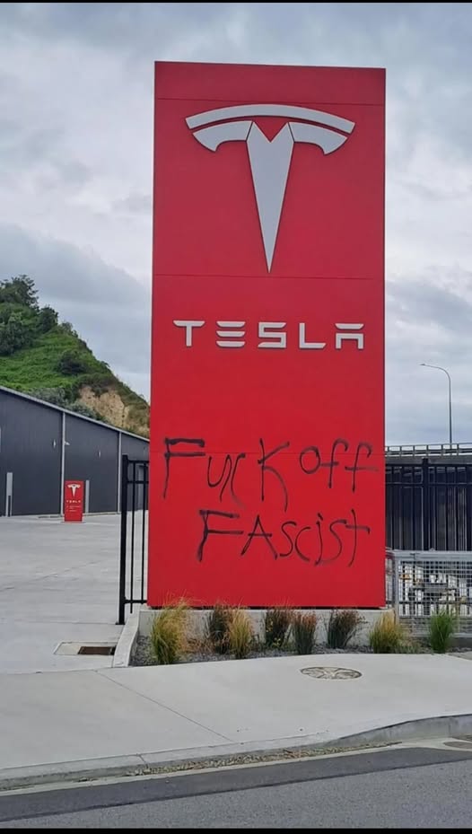The meme features a photo of a Tesla car charging station with a sign that has been vandalized with the words "F**K OFF" and "F**K TESLA" in graffiti. The sign's original text has been altered to include these phrases, suggesting a strong negative reaction to the company.