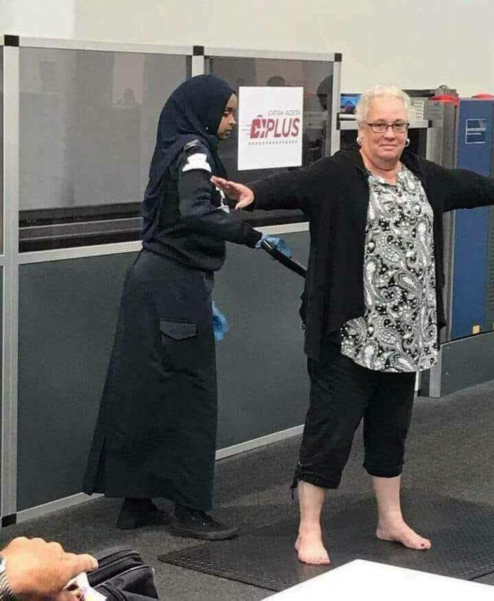The meme features a photo of a woman in a hijab helping an older woman with her yoga pose. The older woman is standing on one leg with her arms outstretched, while the woman in the hijab is holding her arms and providing support. The text "I'm not helping, I'm just making sure you don't fall on your face" is overlaid on the image.