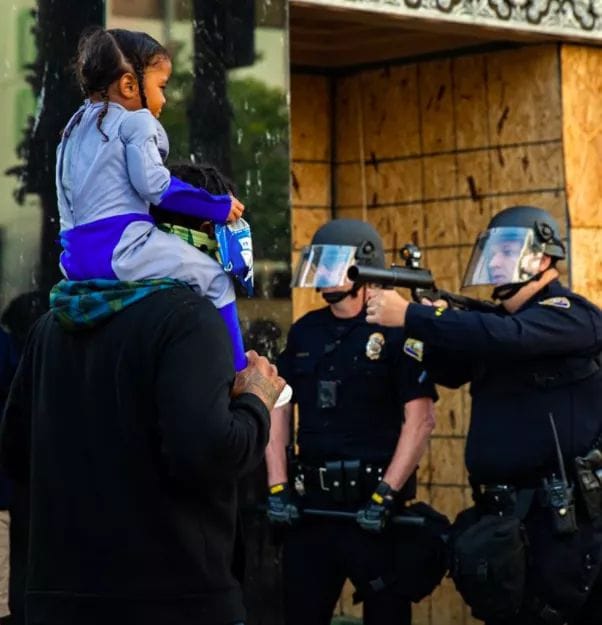 The meme depicts a police officer (a "cop") trying to take a selfie with a child, but the child is holding the cop's gun and the cop is trying to wrestle it away. The image is likely captioned "When you try to take a selfie with a kid but they have other plans". The humor comes from the absurdity of the situation and the unexpected twist on a typical selfie scenario.