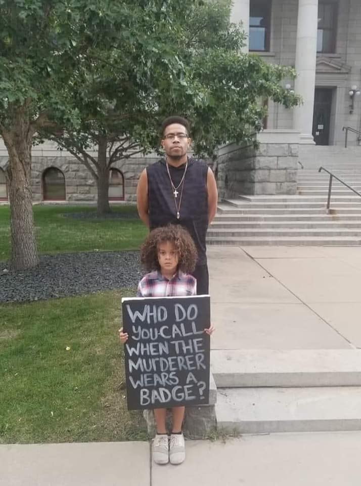 This meme features a photo of a man and a young boy standing on the steps of a courthouse or similar building. The boy is holding a sign that reads "I can explain" in a childlike handwriting, implying that he is trying to justify or explain something.