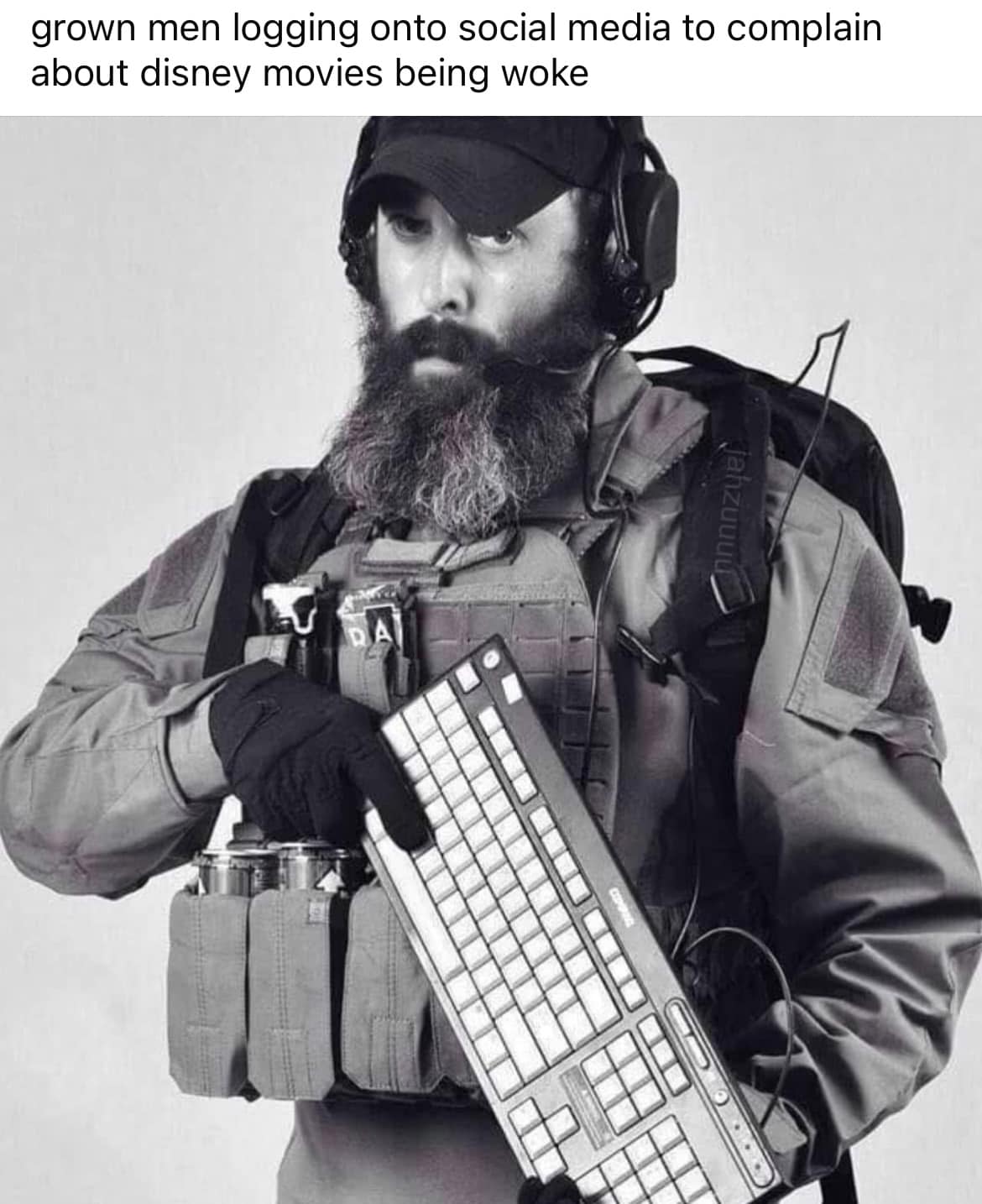 The meme is a humorous image of a man dressed in military gear, holding a keyboard and wearing a headset. The text at the top reads: "When you're a grown man logging onto social media to complain about Disney movies being woke." The image is meant to be ironic, as the man's aggressive appearance is juxtaposed with the mundane task of complaining about Disney movies, implying that he's taking a serious issue to a social media platform.