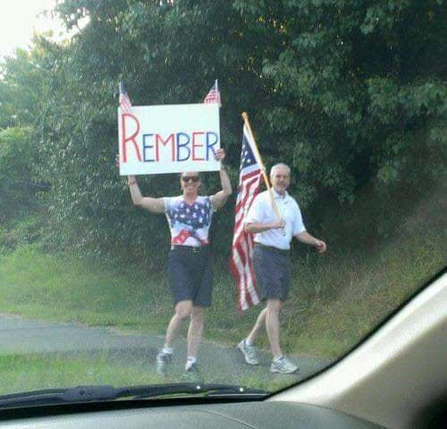 The meme is a photo of two men in shorts and a "Remember" sign, likely referencing the 2020 US presidential election. One of the men is holding a sign that reads "REMEMBER" in bold, red letters, while the other is holding an American flag. The image is likely a humorous commentary on the election or a related topic.