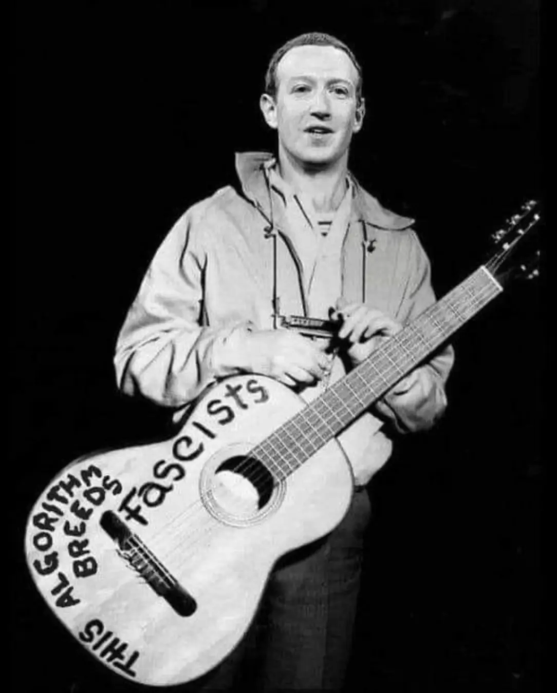 This meme features a photo of a person holding a guitar with a humorous and satirical message. The text on the guitar reads "This guitar kills fascists" and is a reference to the song "The Song of the Sausage People" from the Monty Python's Flying Circus. The image is likely a humorous commentary on the original song's message of resistance and rebellion.