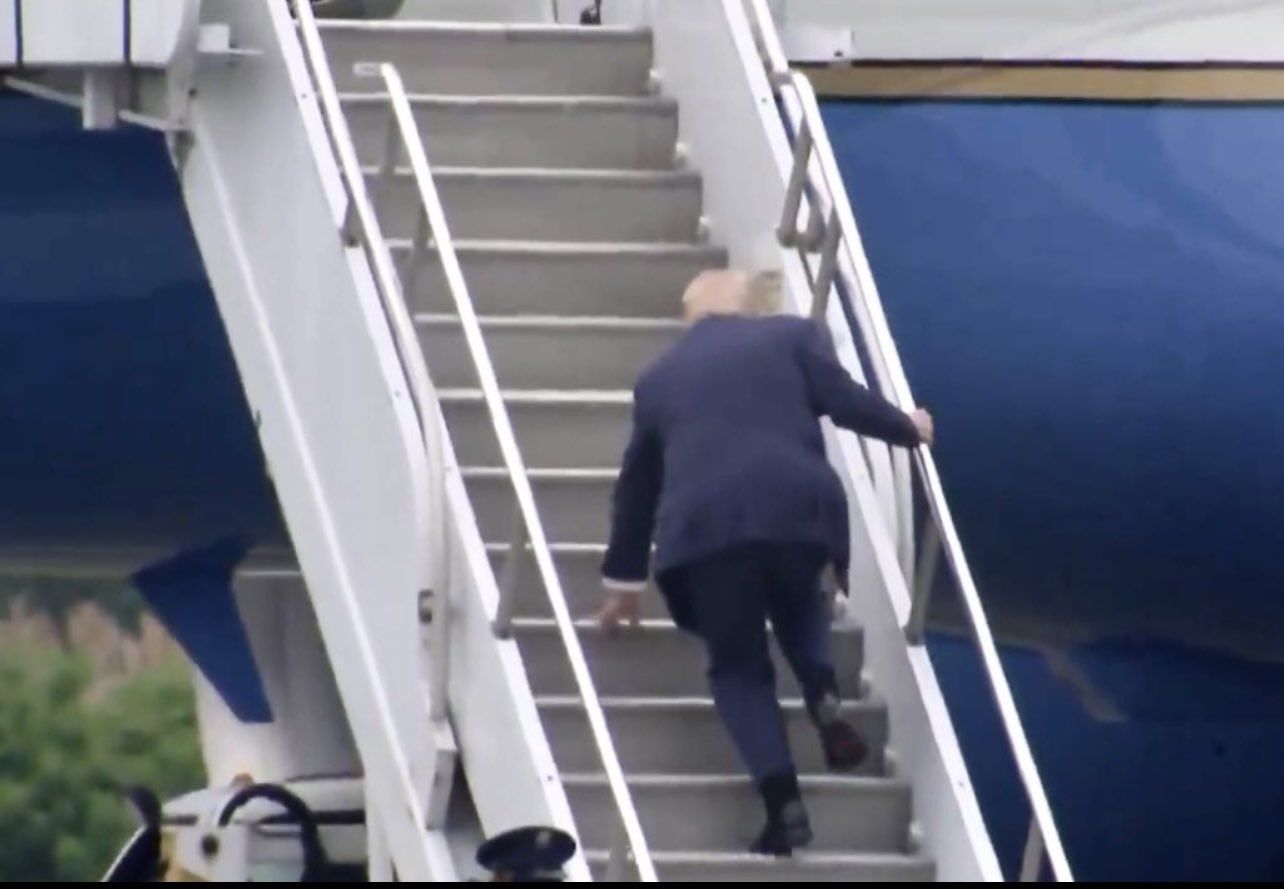 The meme depicts a photo of former US President Joe Biden, 78, stumbling down the stairs of Air Force One, his feet tangled in his own legs. The image is captioned "I'm not going anywhere" in a humorous nod to the president's age and his infamous gaffes. The meme pokes fun at Biden's age and his tendency to make embarrassing mistakes in public.