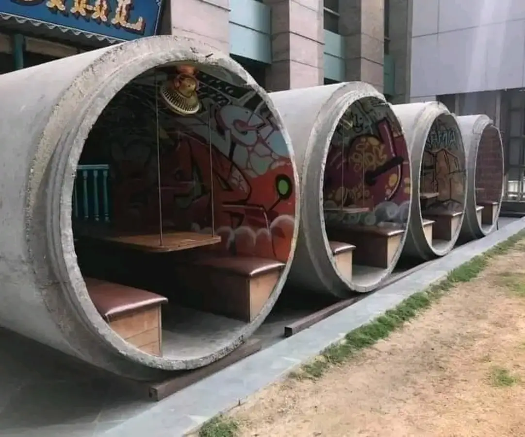 The meme is an image of a row of tunnels made from large concrete pipes, each with a small wooden bench and a desk inside. The text "office spaces of the future" is written above the image. The meme is likely commenting on the idea that some companies are considering using underground tunnels or pipes as office spaces due to rising costs and environmental concerns.