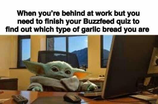 This meme features a character from the Star Wars franchise, Baby Yoda, sitting at a desk with a computer in front of him. The text above him reads "When you're behind at work but you need to finish your BuzzFeed quiz to find out which type of garlic bread you are." The image is humorous because it takes a serious situation (being behind at work) and applies it to a lighthearted and relatable scenario (taking a BuzzFeed quiz).