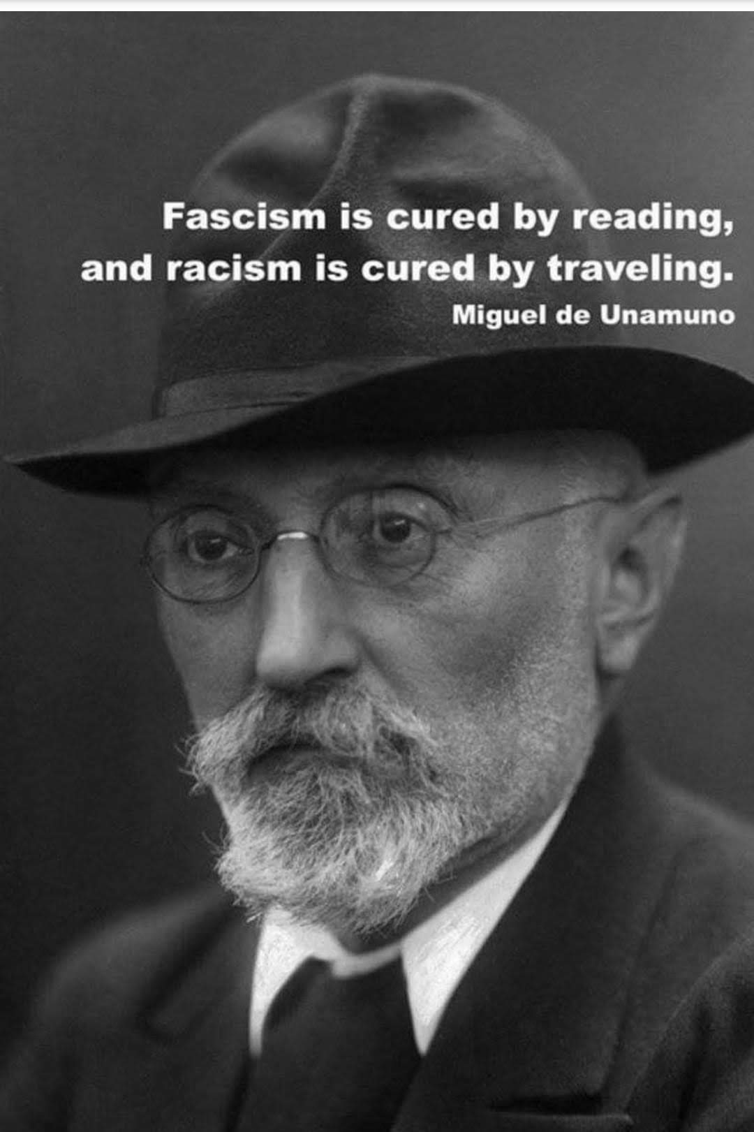 The meme is a black-and-white image of a man with a thick, white beard and a fedorah hat. He is wearing a suit and a tie, and his expression is serious. The text superimposed over the image reads: "Fascism is cured by reading, and racism is cured by traveling. -Miguel de Unamor".