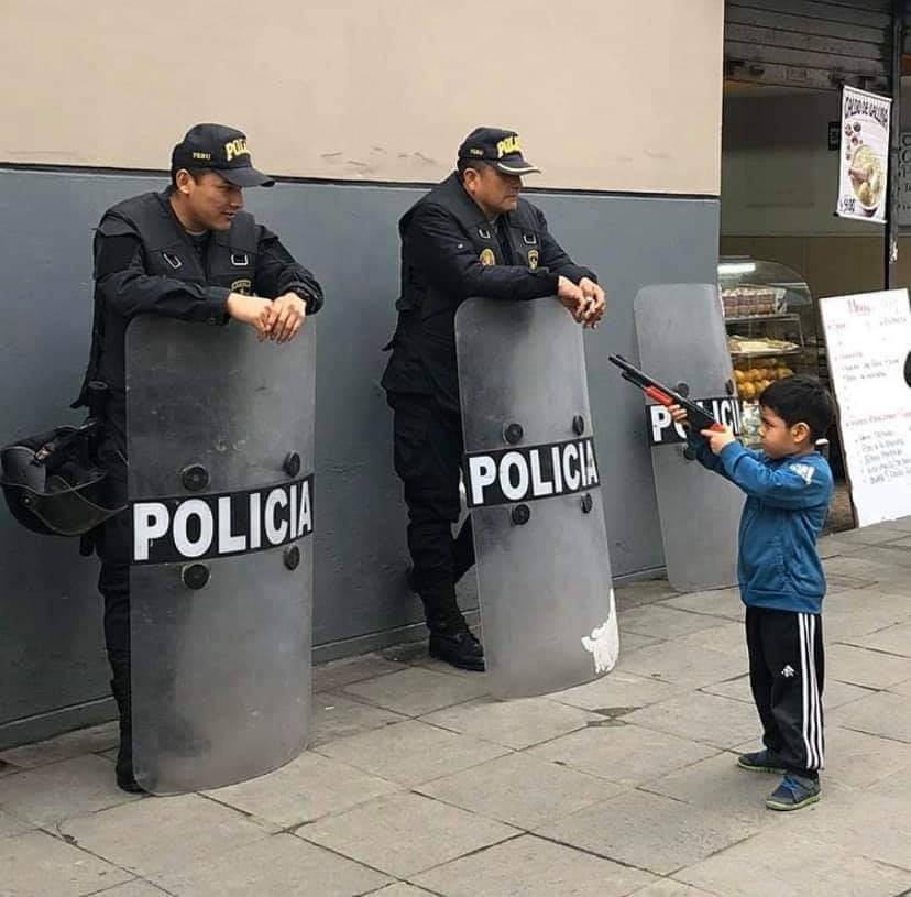 The meme features a young boy, likely in a Latin American country, pointing a toy gun at two police officers. The boy is saying "I'm a cop" in Spanish, "Soy un polico". The image is likely meant to be humorous or ironic, as it's unlikely a child would be able to carry a real gun, let alone be a police officer.
