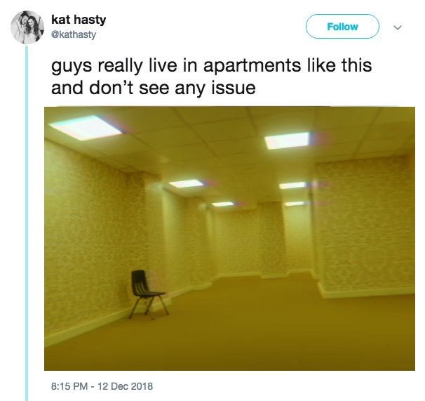 The meme is a screenshot of a Twitter post. The text reads: "guys really live in apartments like this and don't see any issues". The image is a photo of a dimly lit, empty hallway with a chair in the center of the room. The walls are a dull yellow, and the lighting is so poor that it's difficult to make out any details.