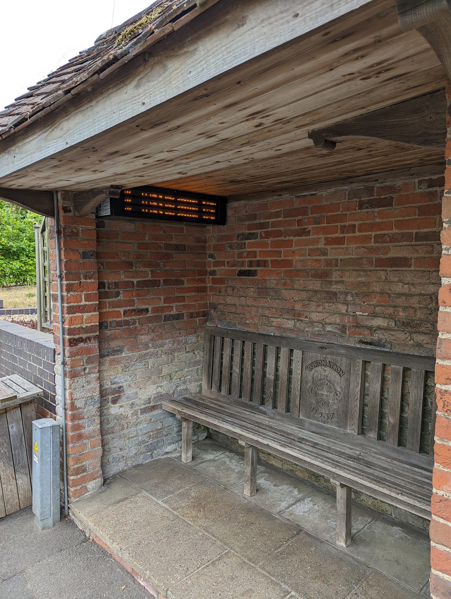 The meme is an image of a small, brick-built bus shelter with a wooden bench inside. The shelter is empty, with no signs of recent use. The text on the shelter's sign reads "2-3 minutes" and "2-3 minutes" again, implying that the bus has been delayed or is not coming at all.