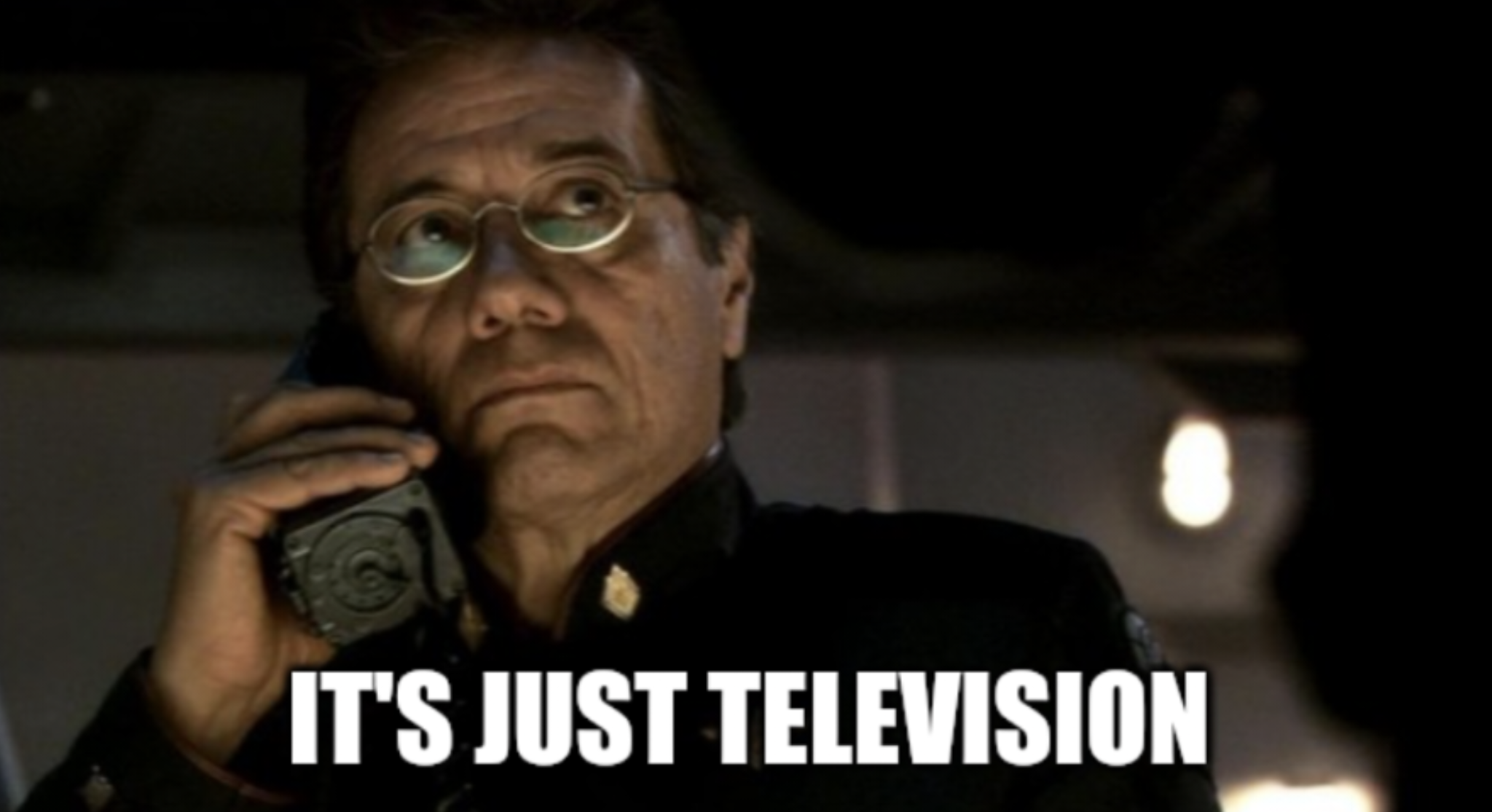 This meme features a still image from the TV show "Firefly" of a character, Captain Mal, holding a phone and looking concerned. The text "It's just television" is overlaid on the image, implying that the character is trying to reassure someone that a situation is not as serious as it seems. The phrase is often used to downplay a situation or to make someone feel better.