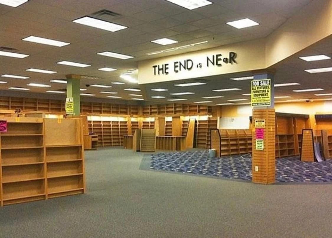 The meme is a photo of a nearly empty, abandoned bookstore. The image is captioned "The End is Near" in a bold, playful font. The caption is a humorous reference to the store's closing, implying that the store's demise is imminent.
