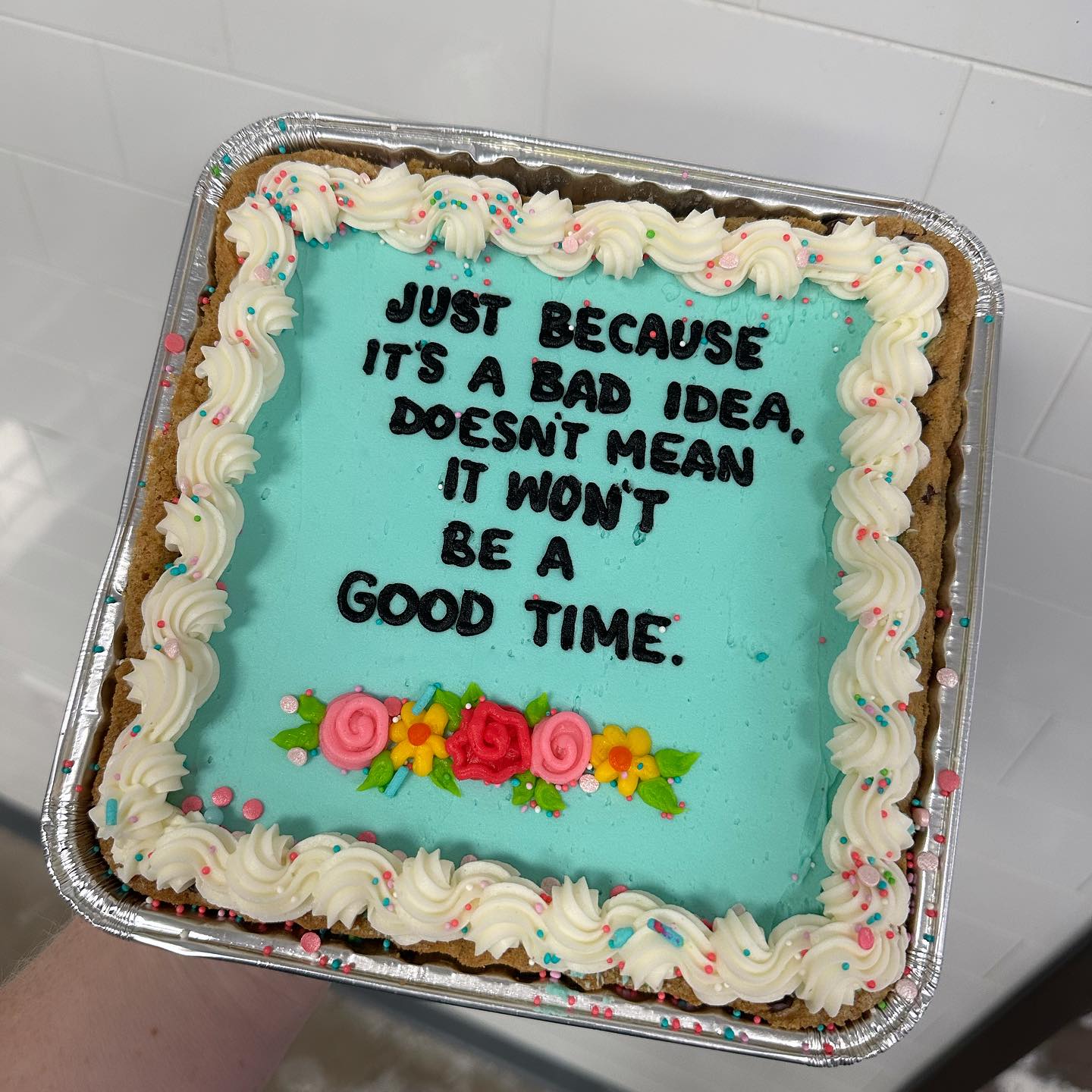 This meme is a humorous take on a common phrase. The image is a picture of a cookie cake with a message written in frosting: "It's a bad idea, but let's do it anyway."