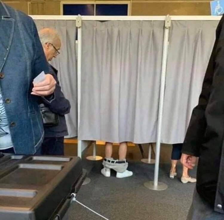 The meme is an image of a person in a voting booth, but they're not actually voting - they're instead playing with their phone, hiding behind the curtain. The text "I'm not voting, I'm just here for the free snacks" is often added to the image, implying that the person is only interested in the food provided at the polling station.