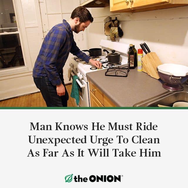 The meme features a photo of a man standing in a kitchen, staring at a stove with a look of confusion and frustration. The image is accompanied by the text: "Man knows he must ride unexpected urge to clean as far as it will take him". The joke is that the man is so overwhelmed by his cleaning urge that he's willing to go to extreme lengths to complete the task.