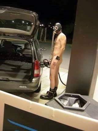 This meme features a person wearing a gas mask and a pair of shorts, standing next to a car with the gas pump still in the car's gas tank. The image is captioned "When you're trying to get gas but you're still on fumes". The meme is likely referencing a situation where someone is running low on fuel and is struggling to get enough to fill up their car.