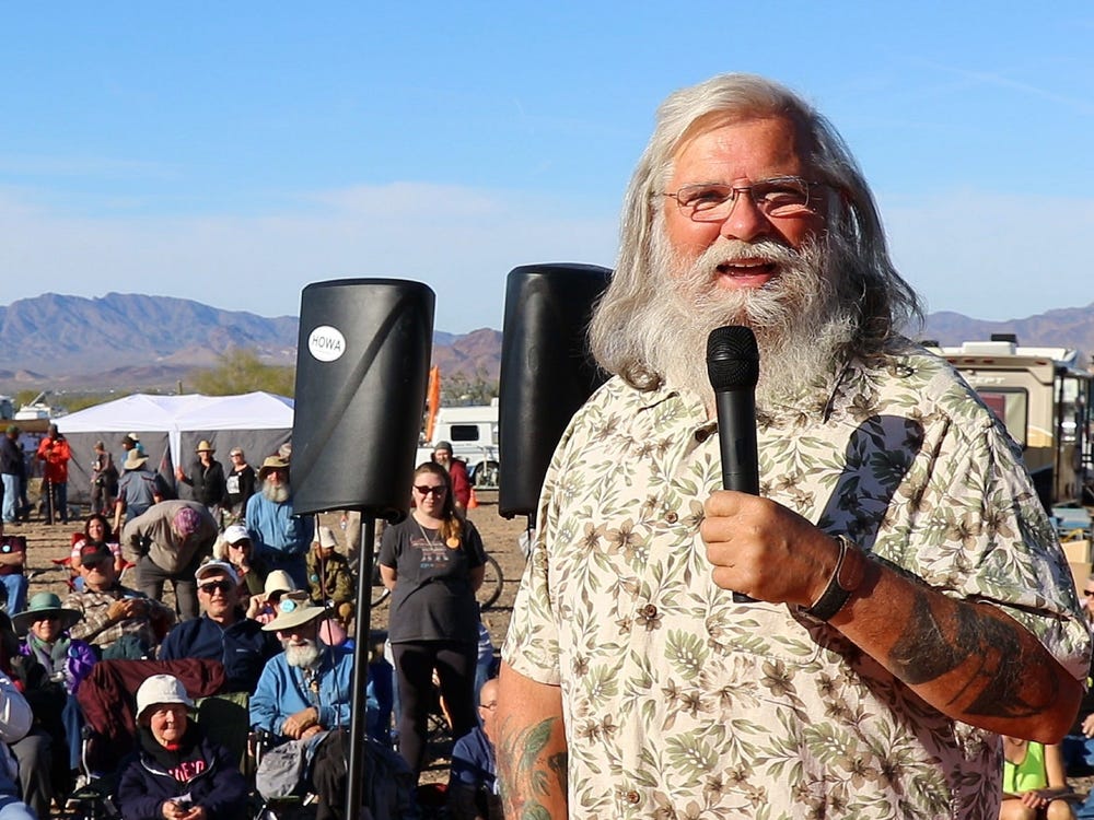 This meme is an image of a man with a long white beard and a Hawaiian shirt, holding a microphone and speaking to a crowd of people. The image is captioned "I'm not arguing, I'm just explaining why I'm right".