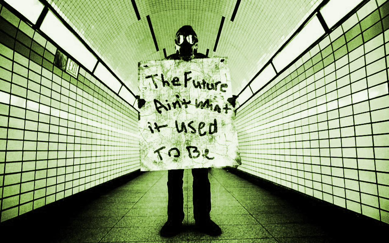 The meme is a photo of a person in a dimly lit room, with a faint glow in the background. The person is wearing a gas mask and holding a sign that reads: "The future ain't what it used to be". The image has a dark and ominous tone, implying a sense of despair and disillusionment.