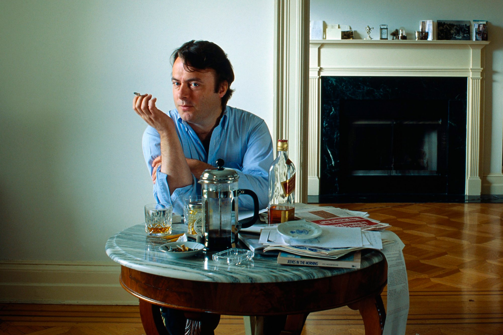 The meme is a picture of a man sitting at a table with a cup of coffee, a cigarette, and a newspaper. He's looking directly at the camera with a mix of boredom and disinterest, as if he's been sitting there for hours. The text "I've been waiting 3 hours for my coffee to get cold" is written in a playful, sarcastic tone.