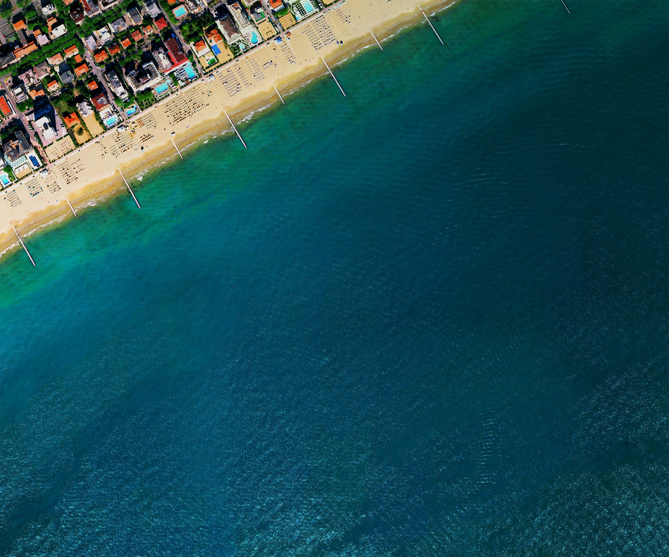 This meme is an image of a beach with a large, dark blue "hole" in the sand, resembling a massive footprint. The text overlaying the image reads "I just found out I'm the 1st in my family to ever graduate college" in a playful, childlike font. The meme is likely referencing a family member's achievement and the "hole" in the sand is a humorous, exaggerated way to visualize the "first" in the family's history.