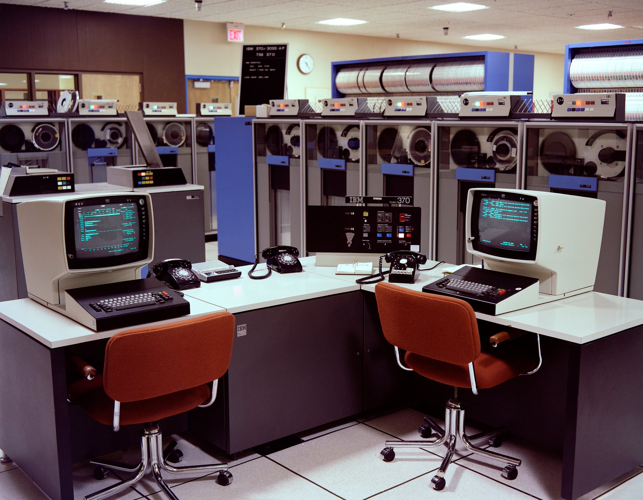 The meme is an image of a 1970s-era computer room, with several old computers and terminals on a desk. The image is captioned "When you're trying to meet a deadline but your terminal is on a 10-minute delay".