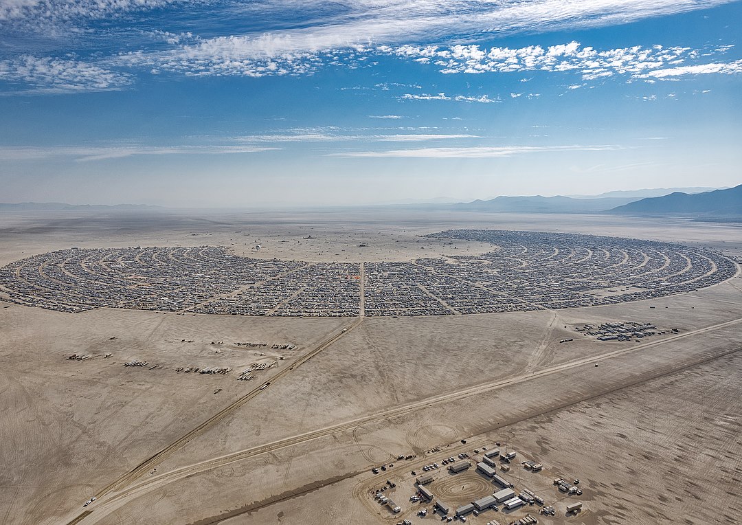 The meme is a picture of a desert landscape with a massive crowd of people in the distance, stretching out in all directions. The text overlay on the image reads "Burning Man" and "I'm not arguing, I'm just explaining why I'm right". The meme is likely referencing the annual Burning Man festival, known for its massive crowds and chaotic atmosphere, and the humorous way that the festival's attendees often argue with each other.