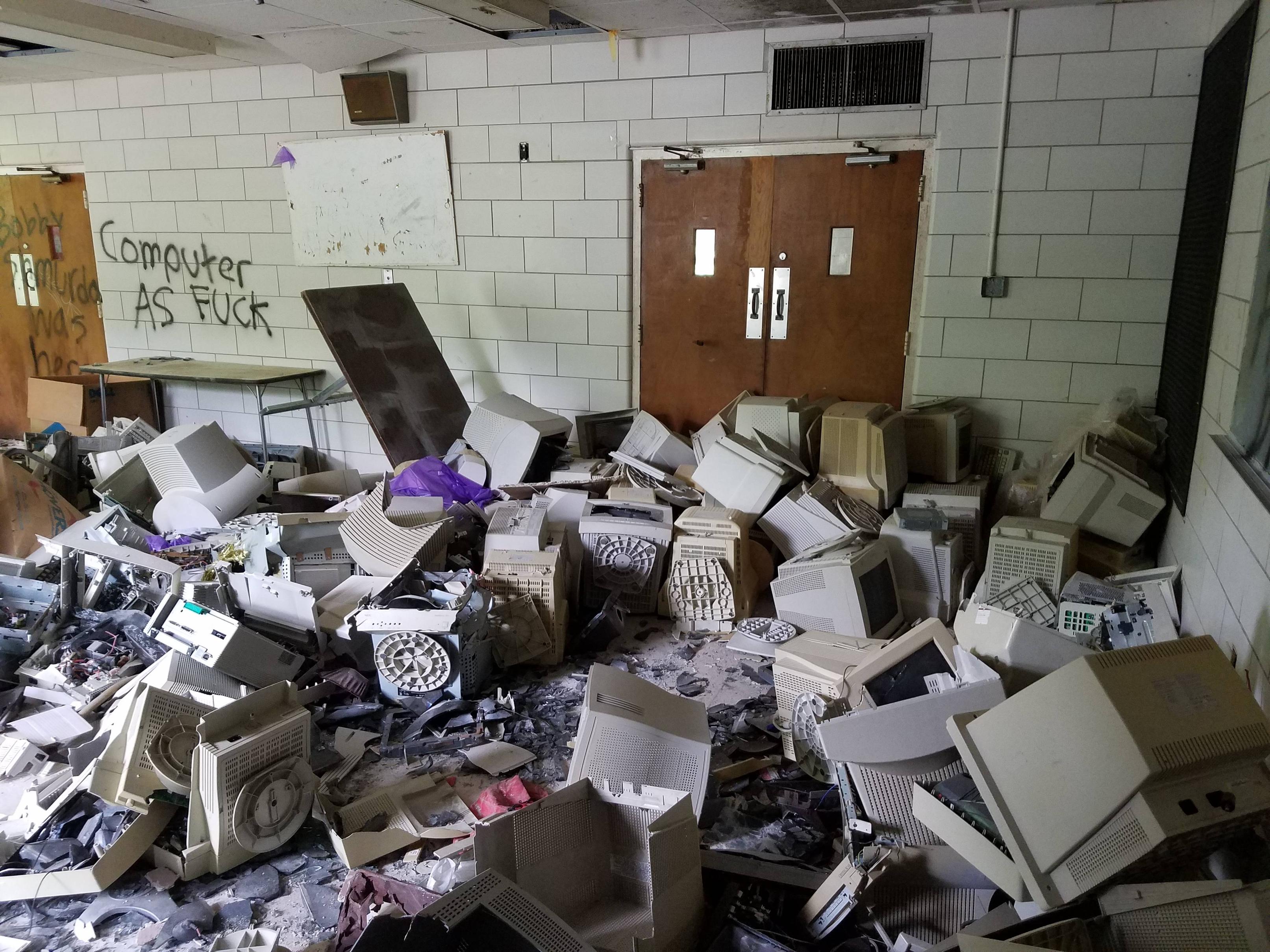 The meme is an image of a chaotic and cluttered room filled with broken computers, wires, and other electronic debris. The text "Computer as f**k" is scribbled on the wall in a messy, graffiti-like font, implying a sense of frustration or anger towards the state of the room. The overall tone is one of chaos and disorganization.