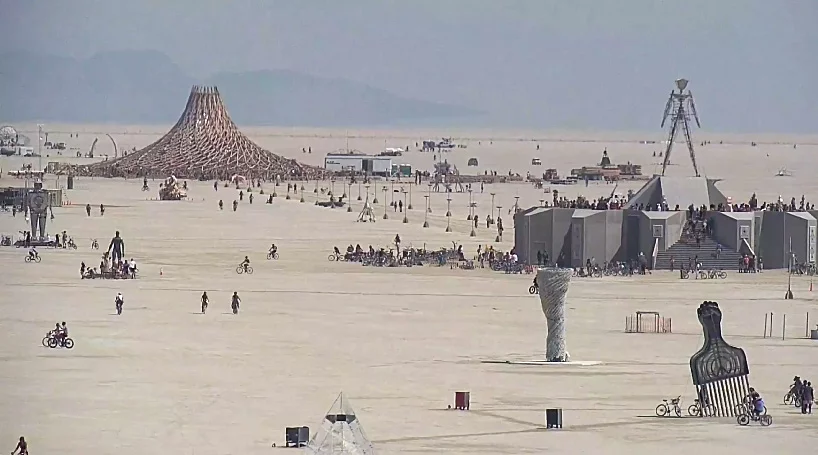 The meme is a screenshot from the Burning Man festival, a popular annual event in the Black Rock Desert, Nevada. The image shows a crowd of people dancing and having fun in the middle of the desert, with a large wooden structure in the background. The text "I just spent 5 days in the desert and I'm still finding sand in weird places" appears in the image, implying that the person is still experiencing the aftermath of the festival.