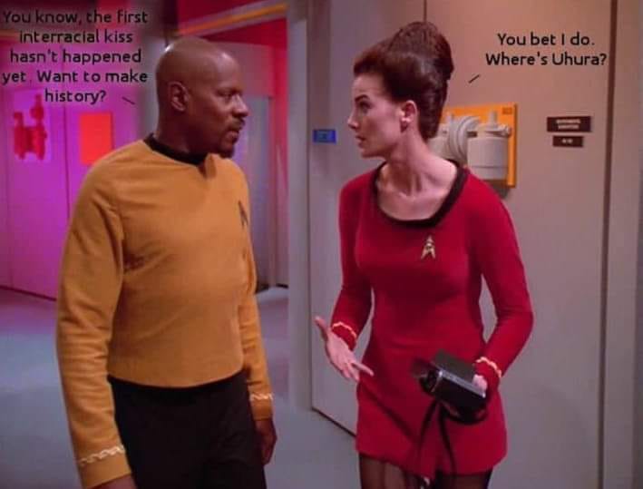 This meme is a still image from the TV show "Star Trek: The Next Generation" featuring characters Deanna Troi and Worf. In the image, Worf is looking at Deanna with a confused expression, and the text "You know the first interracial kiss has not happened yet" is overlaid on the screen. The text is then interrupted by Deanna, who says "In 2-3 sentences, describe this meme for someone who cannot see it" and then continues with "You know the first interracial kiss has not happened yet. Want to make history?"