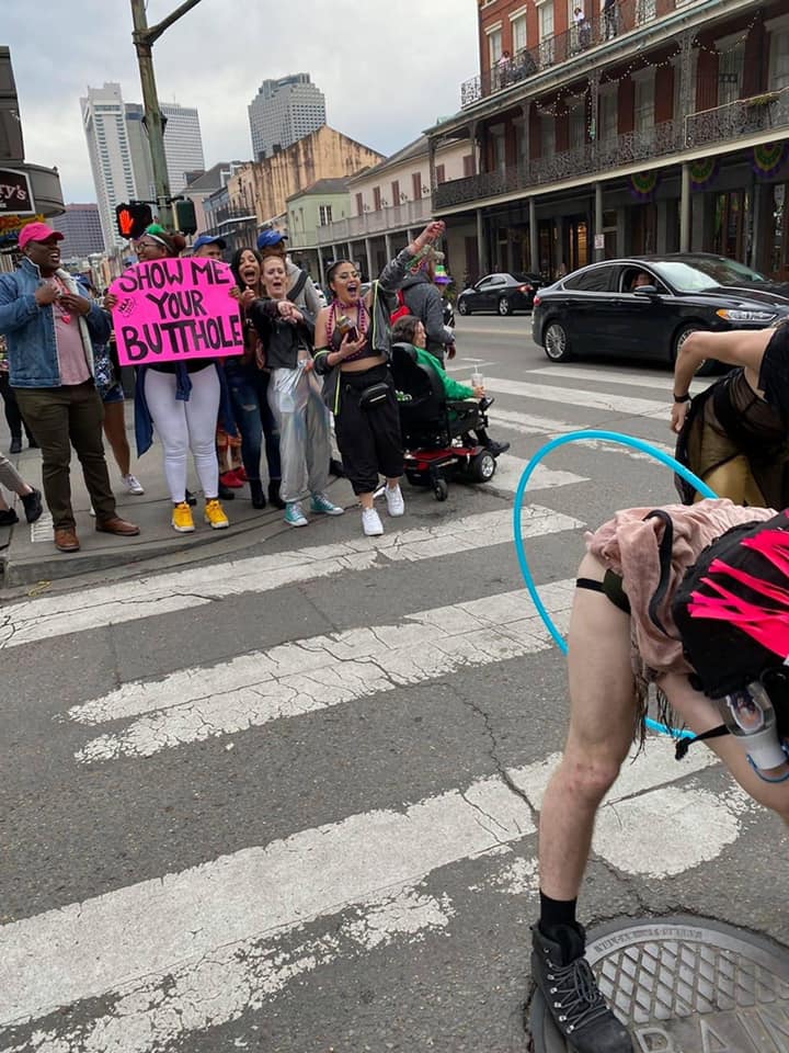 The meme depicts a person in a provocative and humorous situation, likely at a public event or festival, with a focus on their rear end. The image includes the text "Show me your butt" and "Show me your butt hole" written on a sign, which is being held by the person in the center of the image. The overall tone is playful and irreverent, with a dash of silliness and a nod to the idea of being a bit cheeky.
