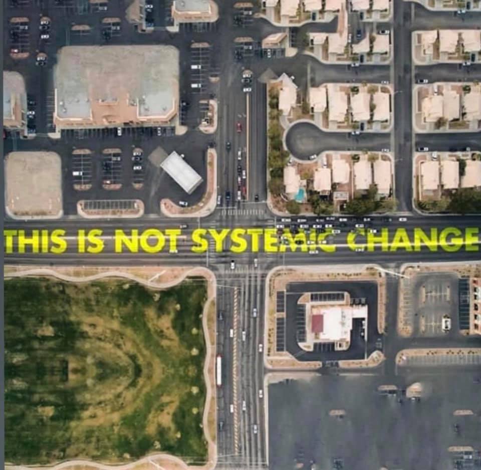 This meme is a satirical image featuring a typical suburban neighborhood with a bland, cookie-cutter design. The text overlay reads "THIS IS NOT SYSTEMIC CHANGE" in a bold, playful font, implying that the lack of diversity and creativity in the neighborhood's design is not a result of a broader societal problem, but rather a mundane, everyday issue.