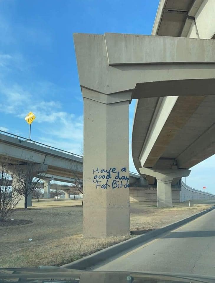 The meme is a photo of a highway overpass with a graffiti tag on the side of the structure. The text reads "Have a nice day" in a sarcastic, illegible handwriting style, implying the opposite sentiment. The phrase is meant to be ironic and humorous, poking fun at the idea of expressing goodwill in a public space.